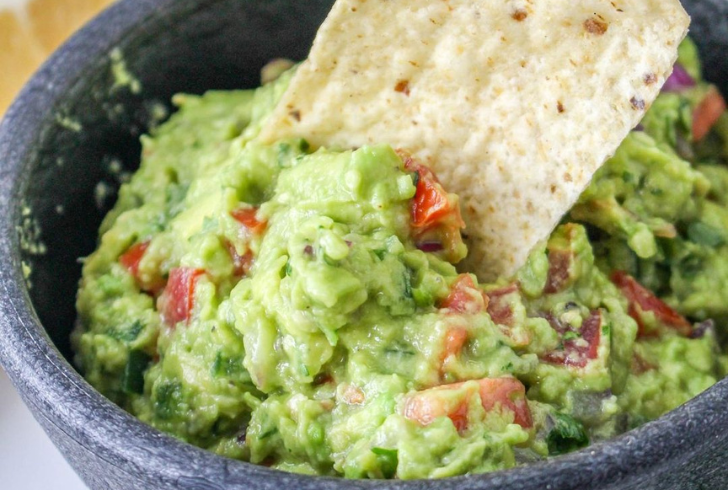 A close-up image of Spicy Guacamole recipe garnished with cilantro and lime wedges.
